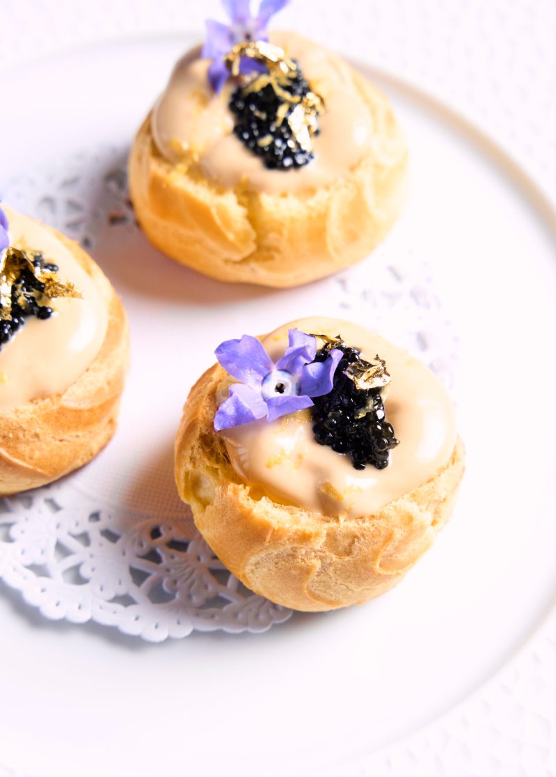 Choux puffs filled with cream and topped with caviar, gold leaf and borage blossoms