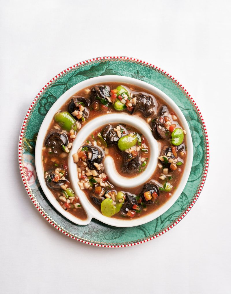 Escargot in sauce bordelaise served in a spiral dish on a green floral plate